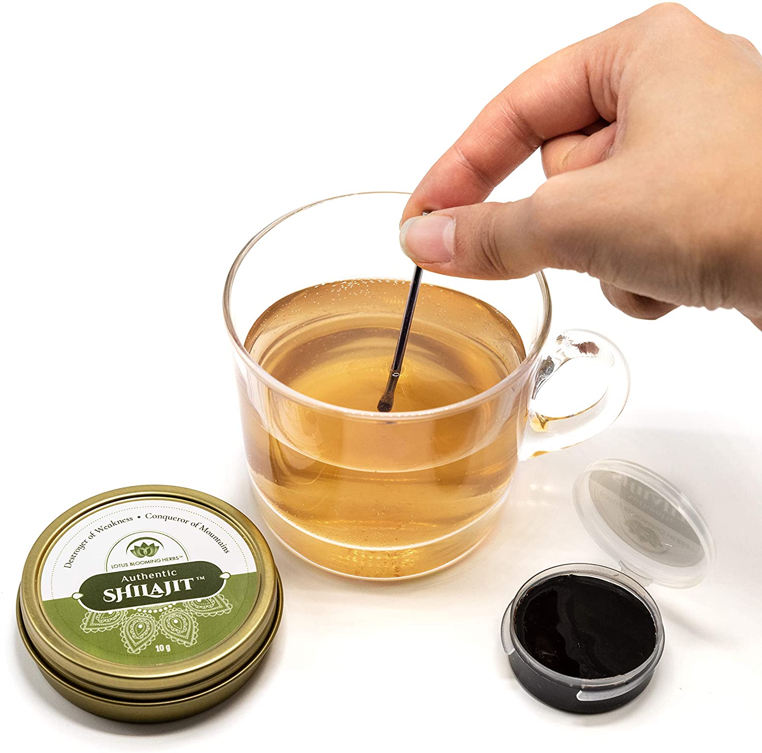 Hand stirring pure natural shilajit in tea with Yoga Nutrition's Lotus Blooming Herbs container nearby.